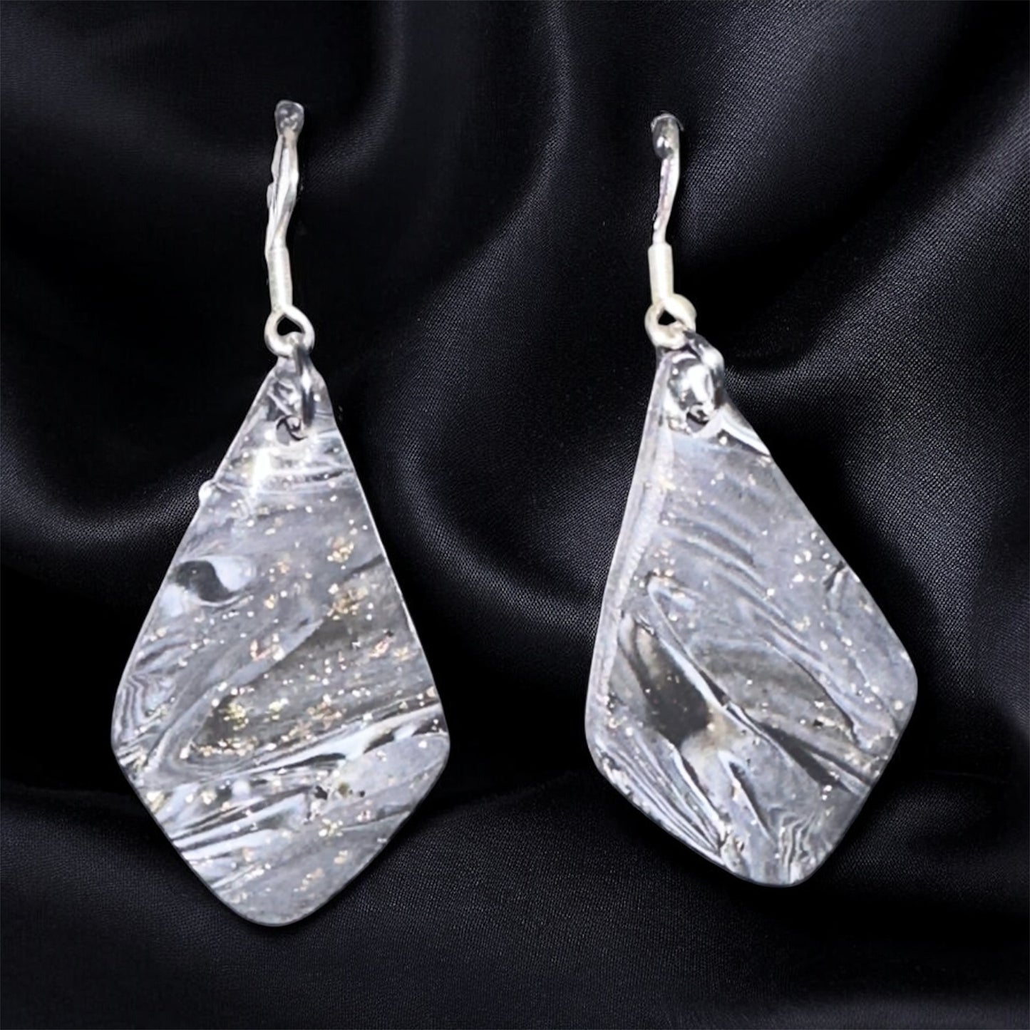 Teardrop-shaped silver earrings on a black satin background