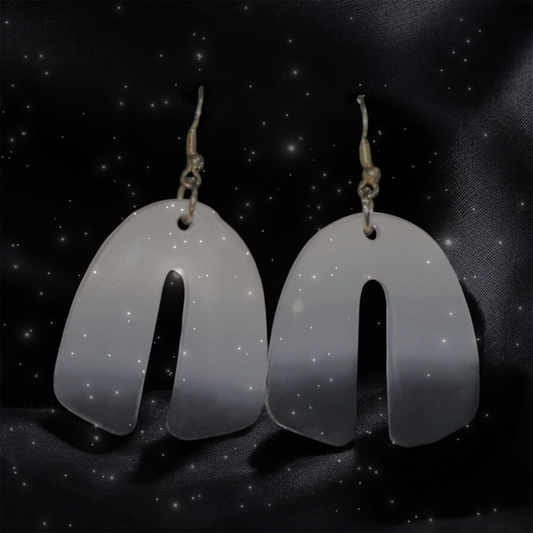 Pair of white earrings on a black background with star-like dots