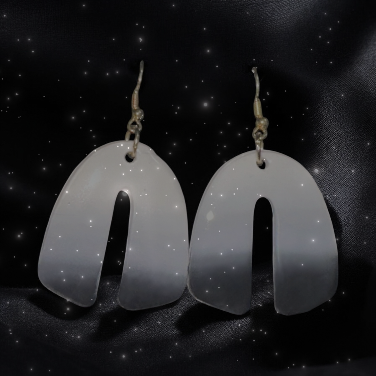 Pair of white earrings on a black background with star-like dots