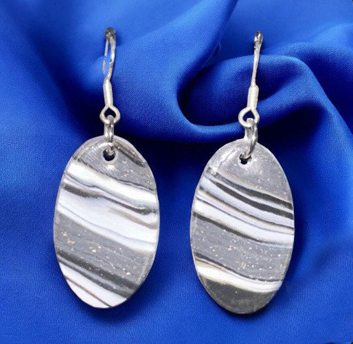Pair of silver earrings with marbled design on a blue fabric background